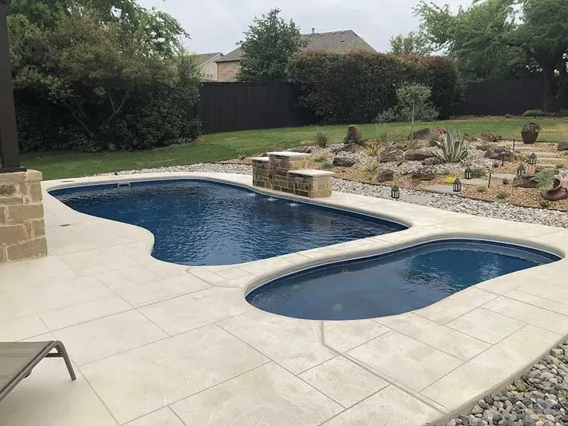 Backyard swimming pool with attached shallow spa, stone patio, and landscaped garden beyond