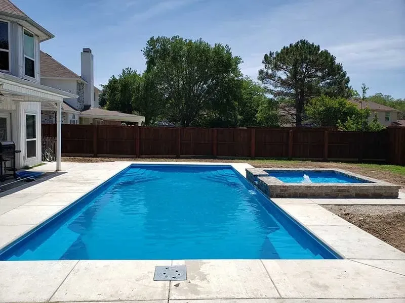 Backyard swimming pool with blue water, white deck, and fenced yard under a clear sky