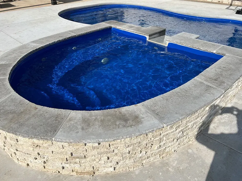 Blue-tiled swimming pool with a curved concrete edge and shallow attached spa outdoors
