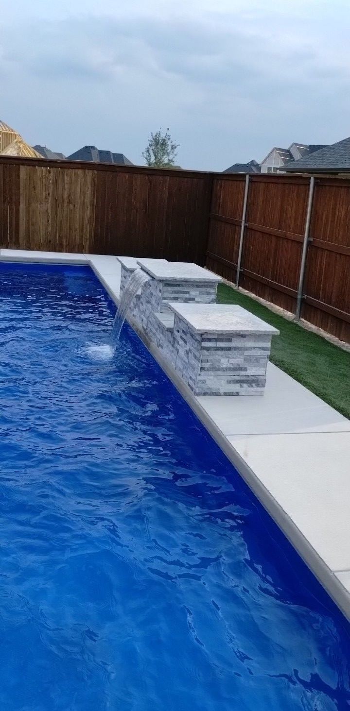 Backyard swimming pool beside a wooden fence with a white deck and gray lounge chairs