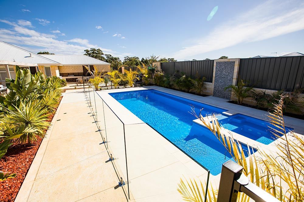 Backyard swimming pool beside a patio with potted plants and a blue sky