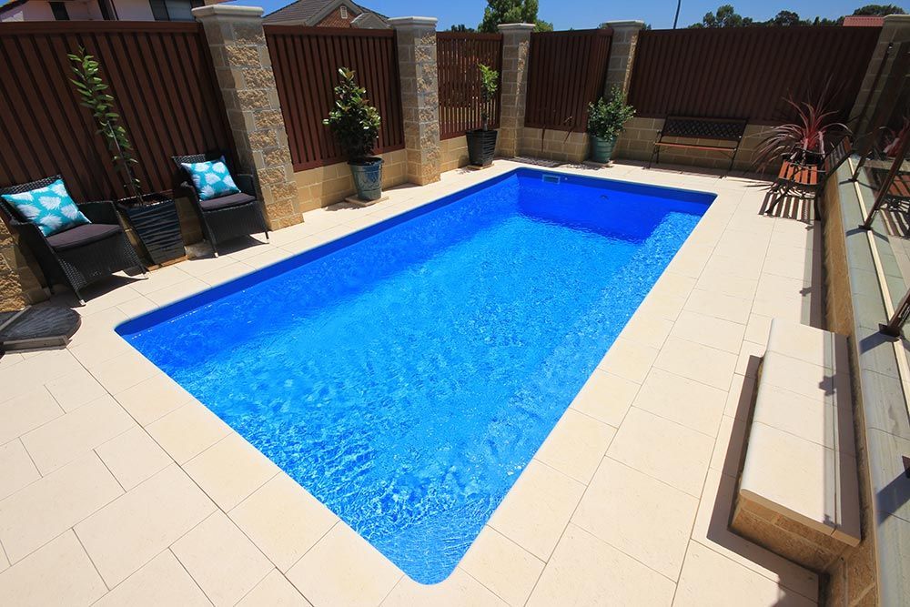 Backyard swimming pool with bright blue water, beige tiles, and wooden privacy fencing