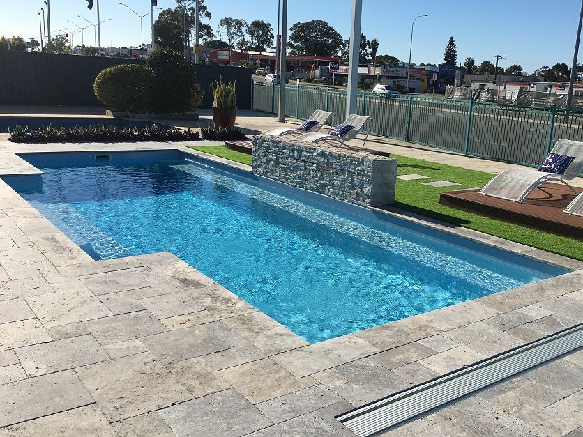 Backyard pool with blue water, stone waterfall feature, and lounge chairs beside a patio