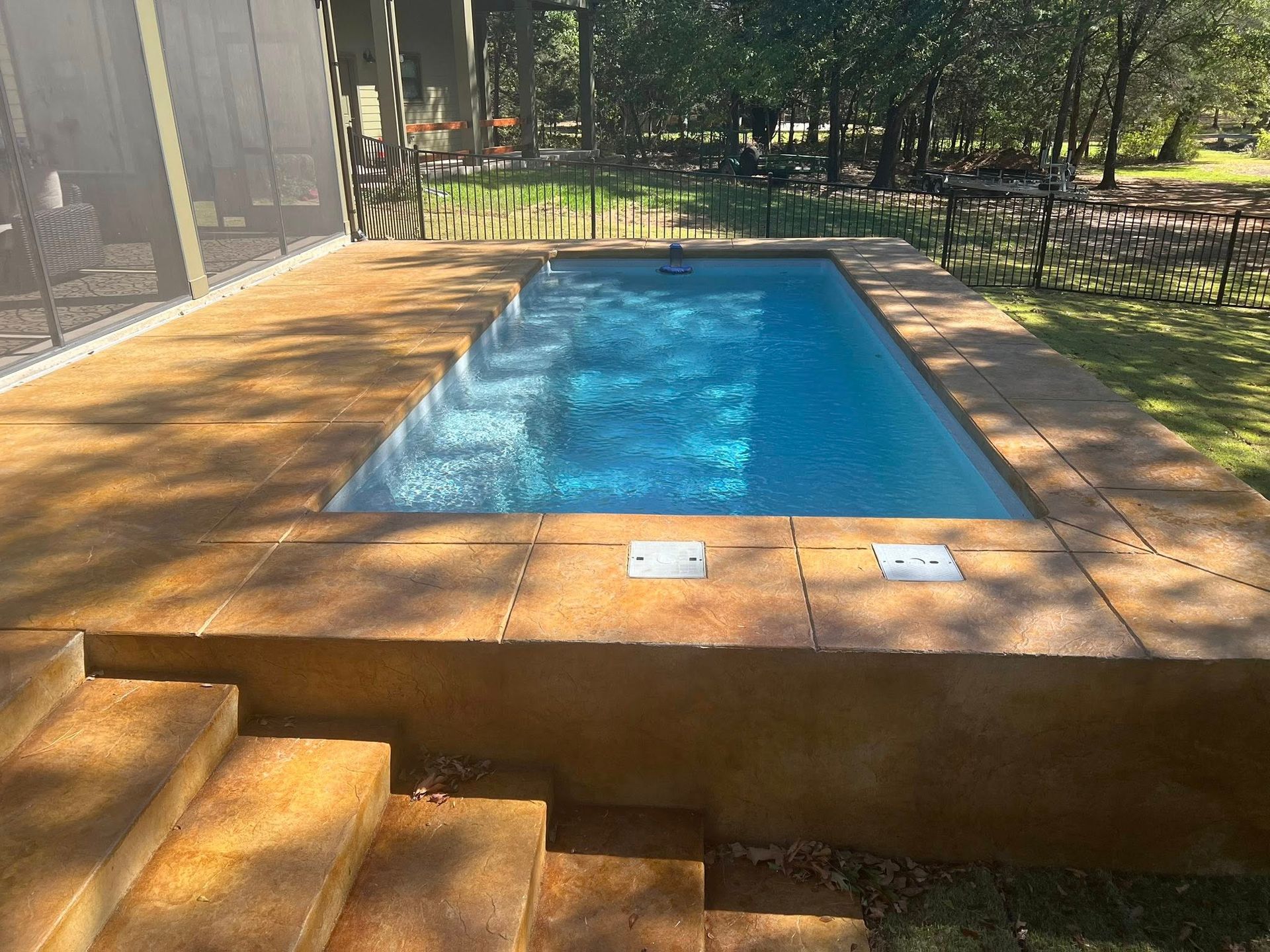 Backyard swimming pool with blue water, surrounded by tan stone decking and steps in the foreground