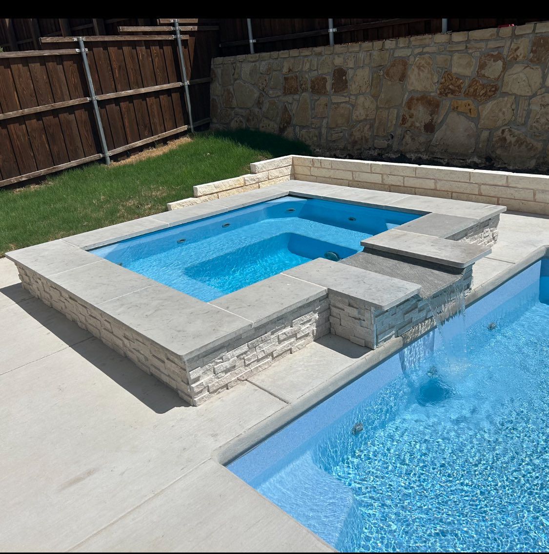 Backyard swimming pool with raised spa, stone coping, and blue water under bright sunlight