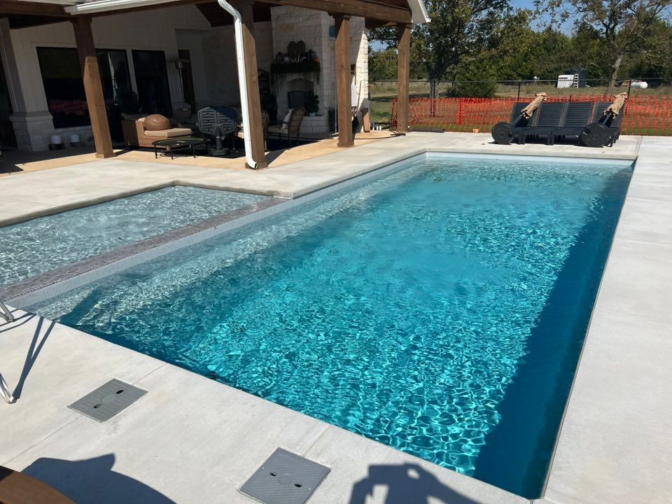 Backyard swimming pool beside a patio and covered seating area on a sunny day