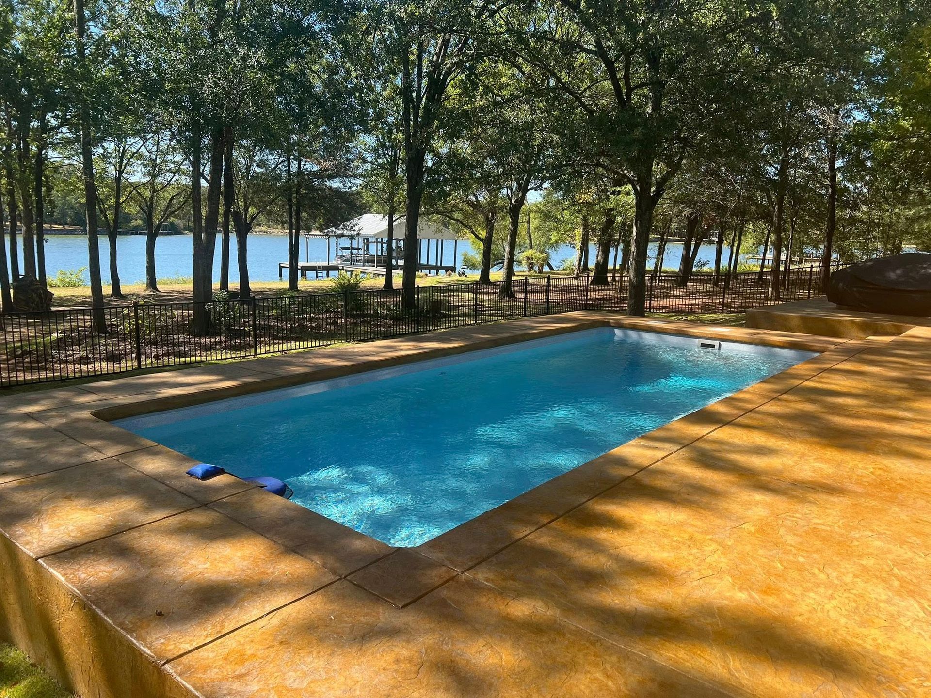 Rectangular blue pool under trees by a lakeside with chairs and umbrellas in the background