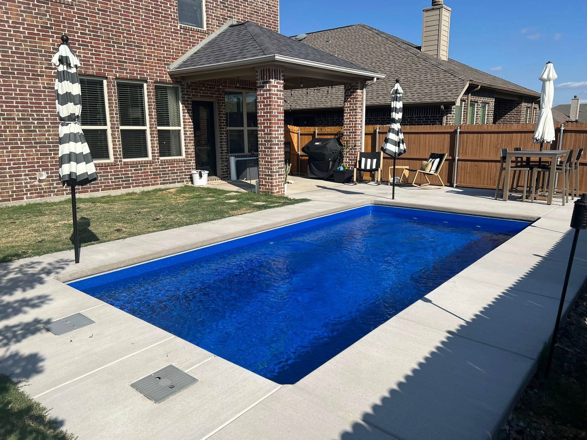 Backyard patio with a small blue pool, stone deck, and covered outdoor seating area