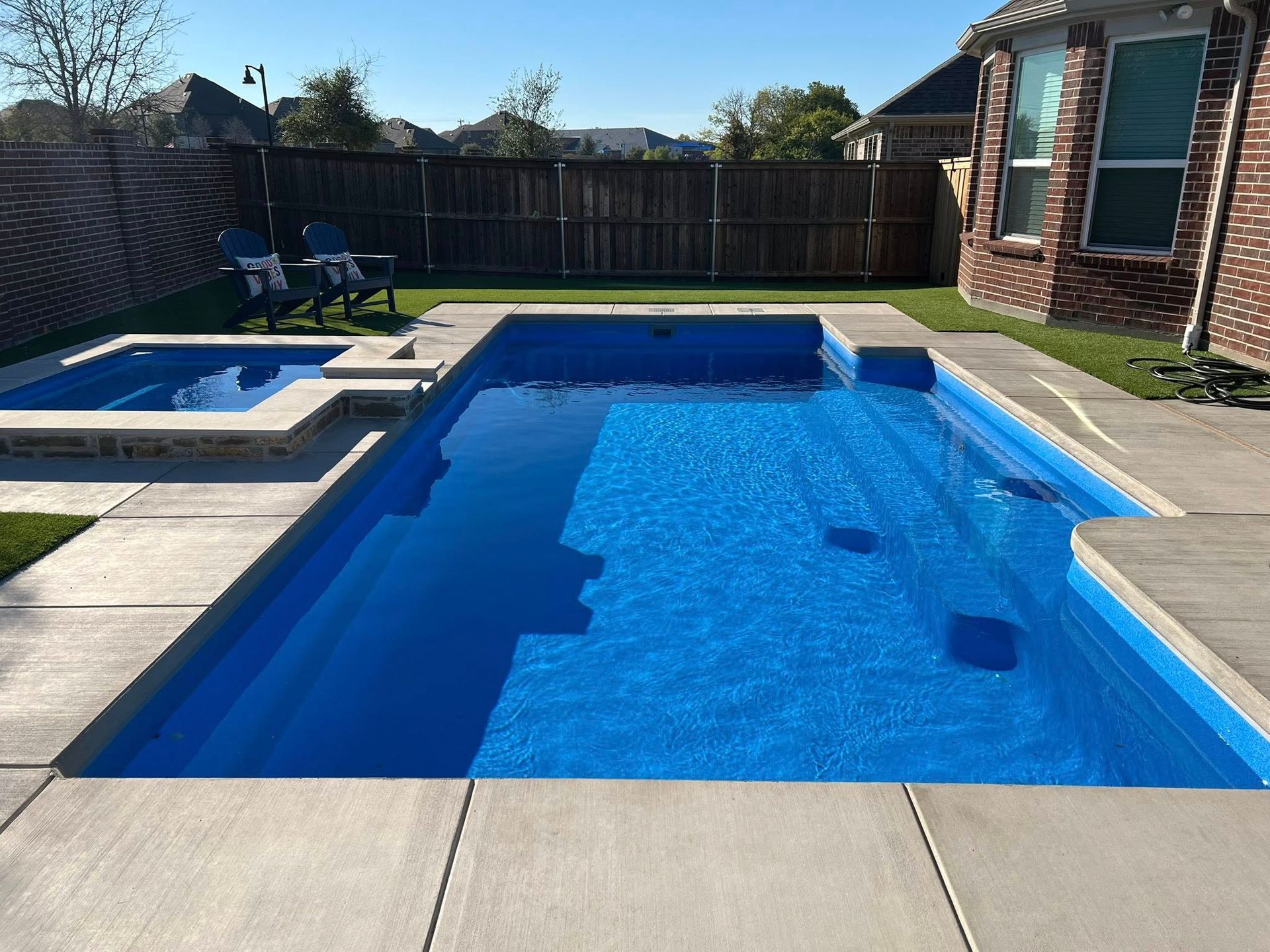 Backyard swimming pool with bright blue water, hot tub, and brick house patio on a sunny day