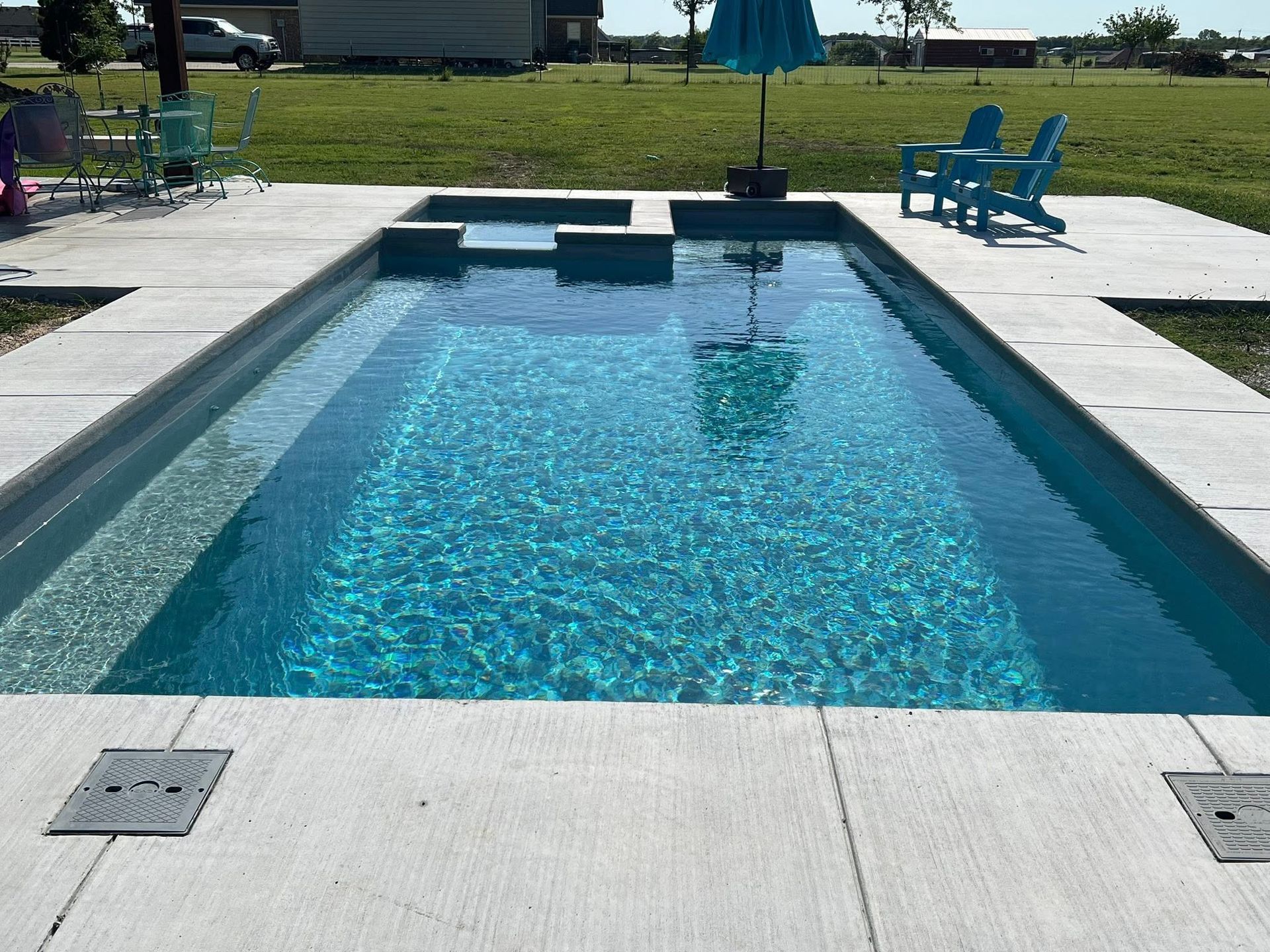 Rectangular backyard pool with blue water, concrete deck, and lounge chairs in the background