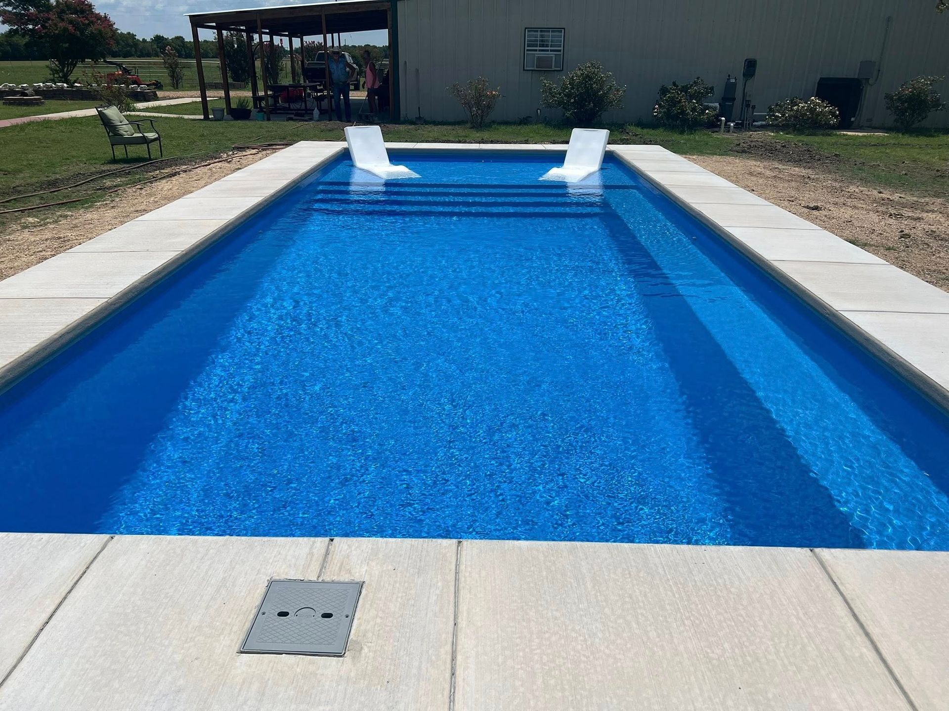 Rectangular outdoor swimming pool with bright blue water and two white pool slides at the far end