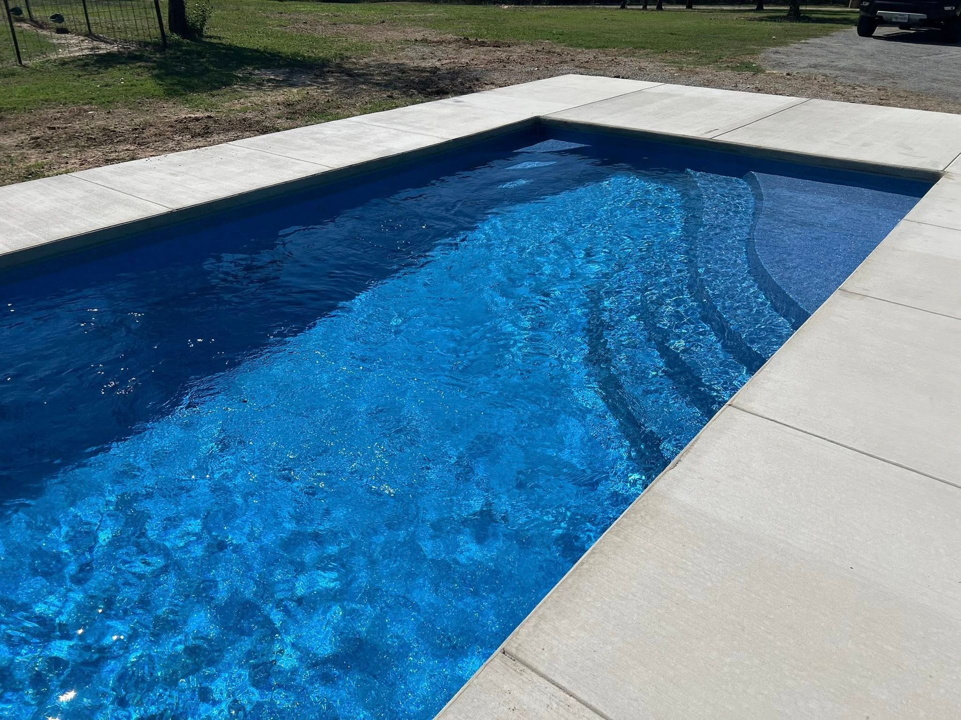 Rectangular outdoor pool with bright blue water and white stone coping