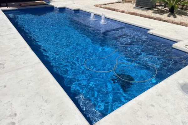 Rectangular blue swimming pool with white stone deck and a small palm in the background