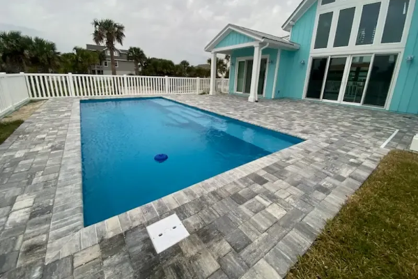 Modern backyard pool with blue water, gray paver deck, white fence, and turquoise house exterior