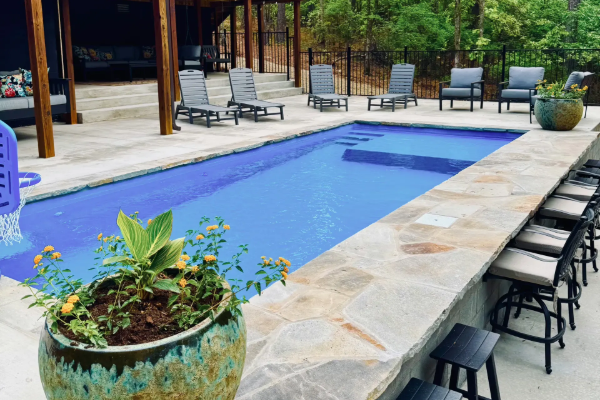 Backyard pool with blue water, stone deck, lounge chairs, and potted plants