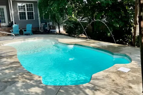 Backyard swimming pool with bright blue water beside a shaded patio and house.