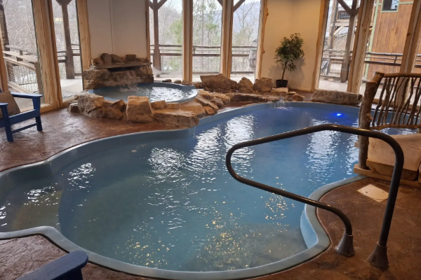 Indoor spa pool with curved blue water, stone hot tub, and large windows overlooking the outside.