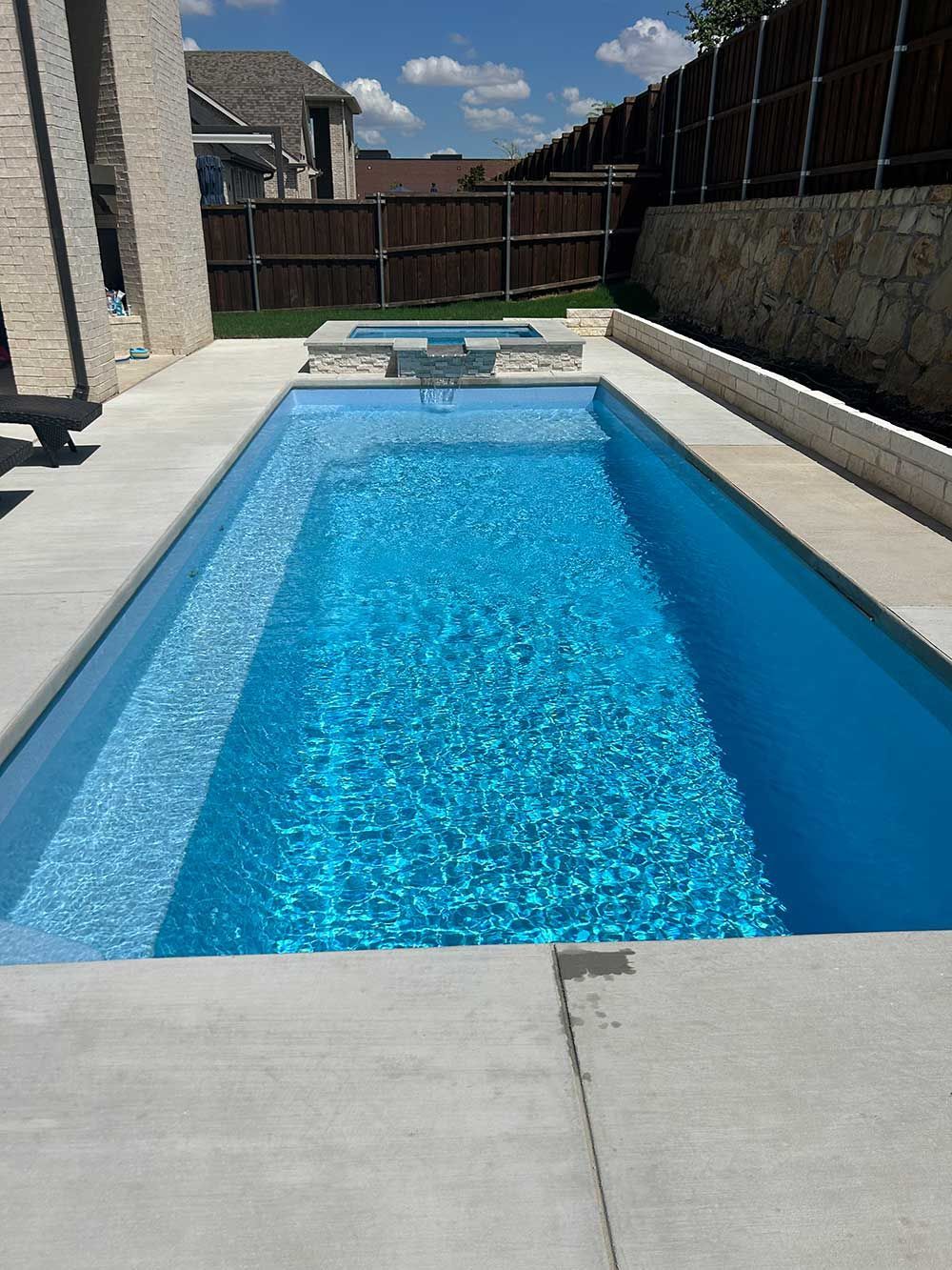 Rectangular backyard swimming pool with bright blue water and concrete deck under a sunny sky
