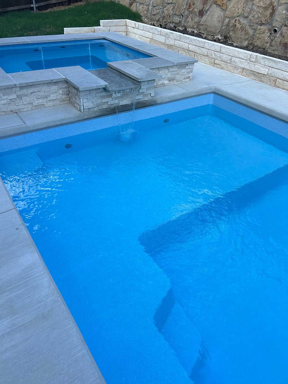 Blue swimming pool with steps and surrounding stone patio outdoors