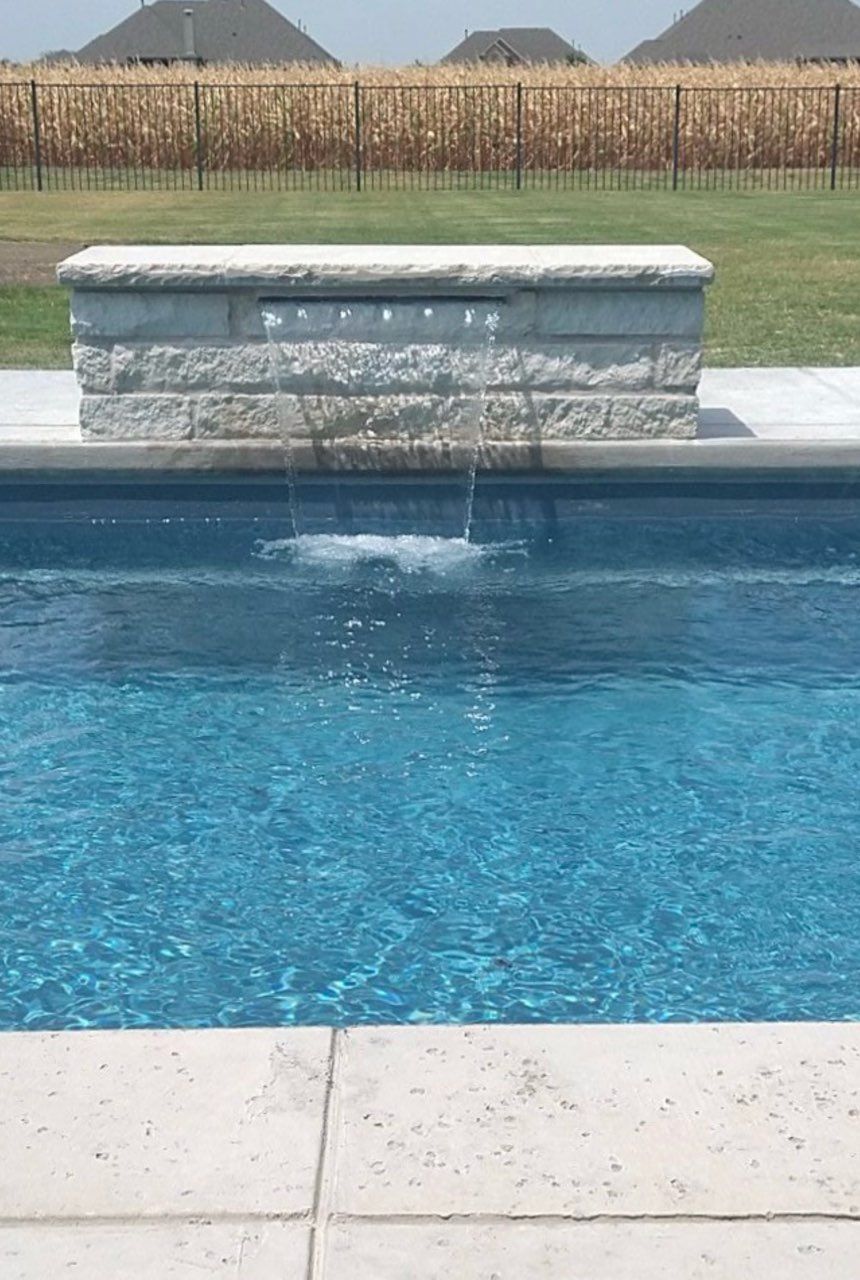 Pool with blue water and a stone spillover fountain in the center, viewed from the deck
