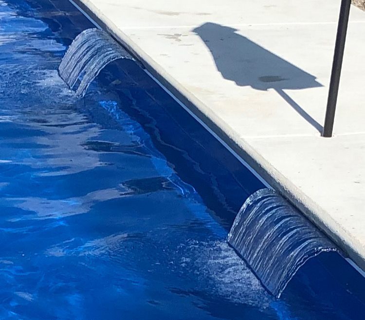 Blue water flowing through a narrow canal beside a concrete deck, with ripples and a shadow overhead