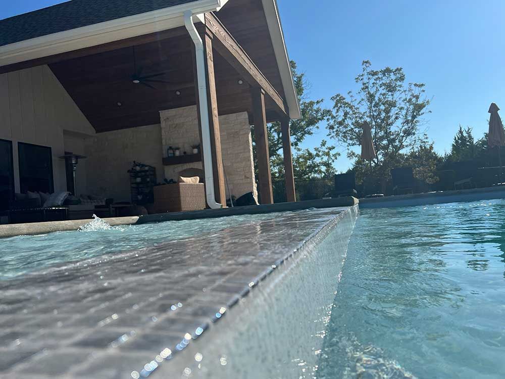 Backyard pool edge with patio and house beside clear blue water