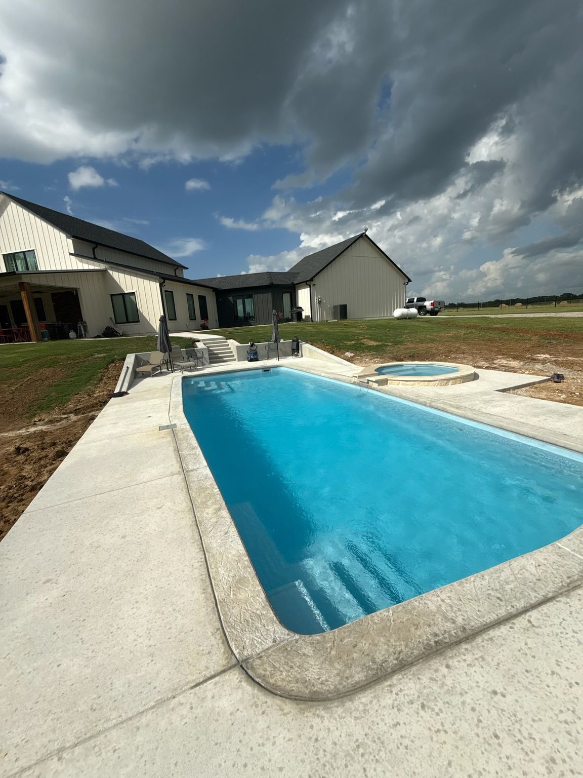 Backyard swimming pool beside a house under a cloudy sky