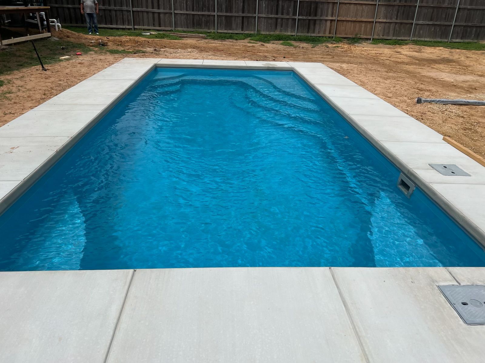 Rectangular backyard swimming pool with blue water, white coping, and a wooden fence around it