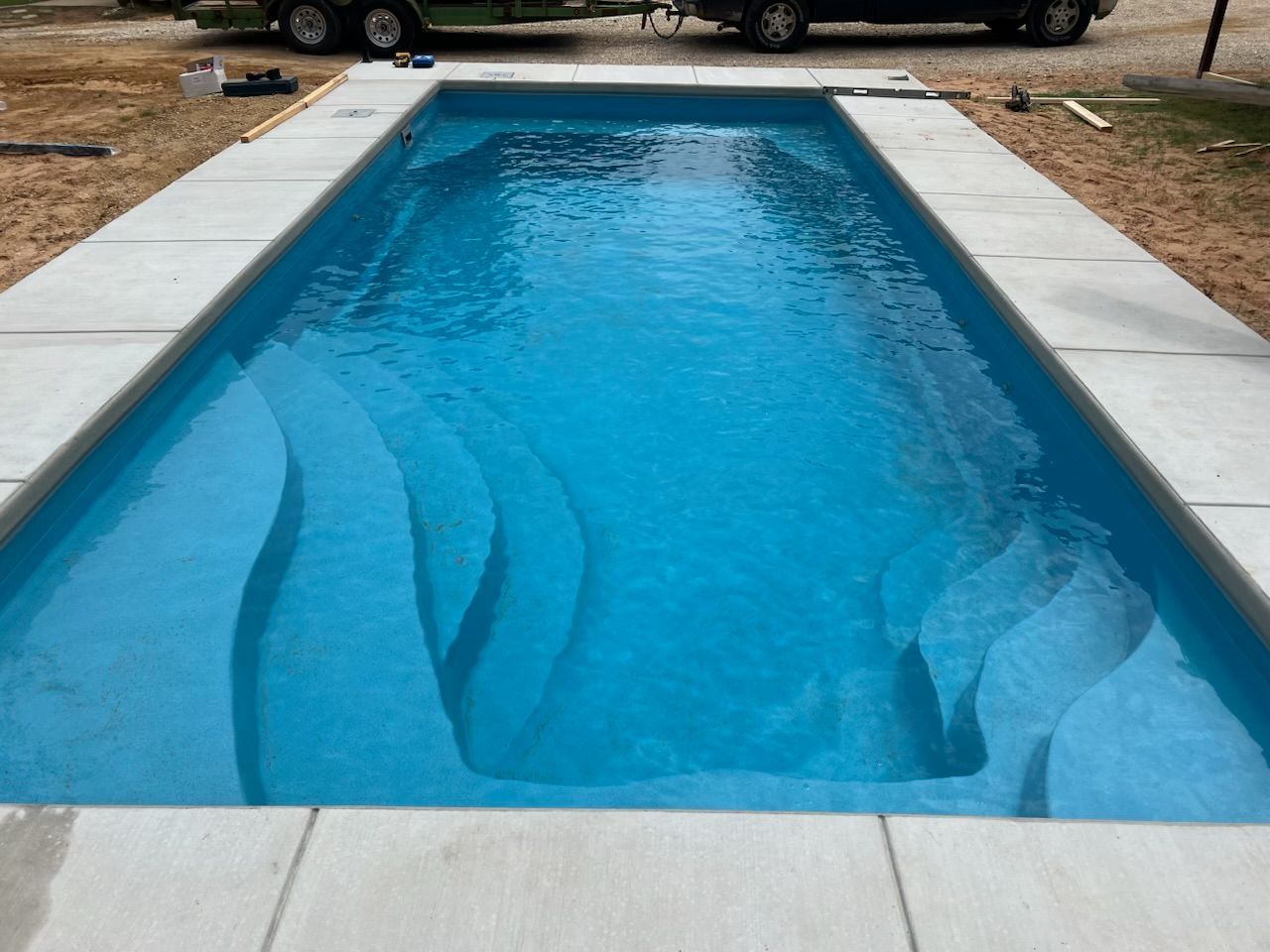 Rectangular backyard swimming pool with blue water and light stone decking