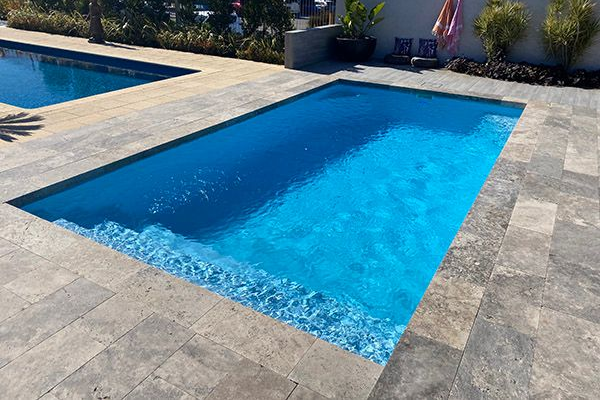 Blue swimming pool with stone deck in a sunny outdoor backyard