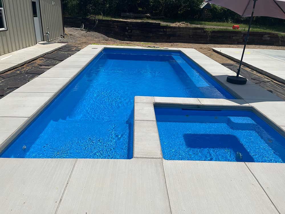 Backyard pool with bright blue water and a shallow spa area beside a concrete deck