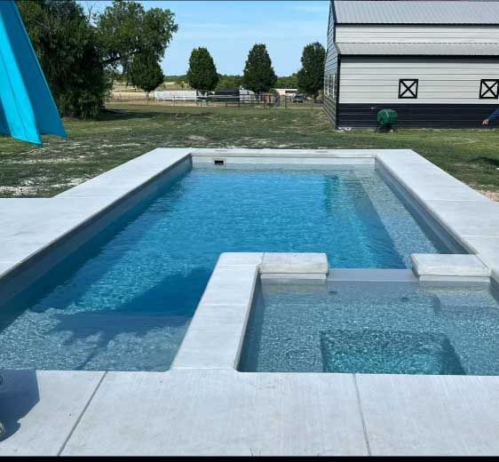 Modern backyard pool with blue water, white stone decking, and a small spa in the foreground