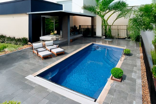 Modern backyard with a blue rectangular pool, lounge chairs, and a covered patio beside a house