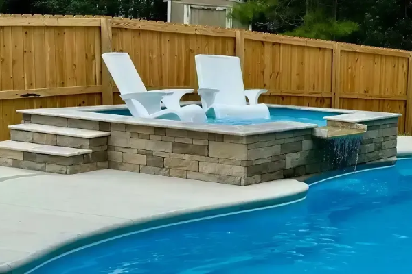 Backyard pool with raised hot tub, stone steps, and two white lounge chairs against a wooden fence