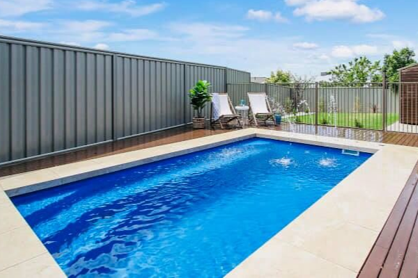 Modern backyard pool with blue water, lounge chairs, and gray privacy fencing