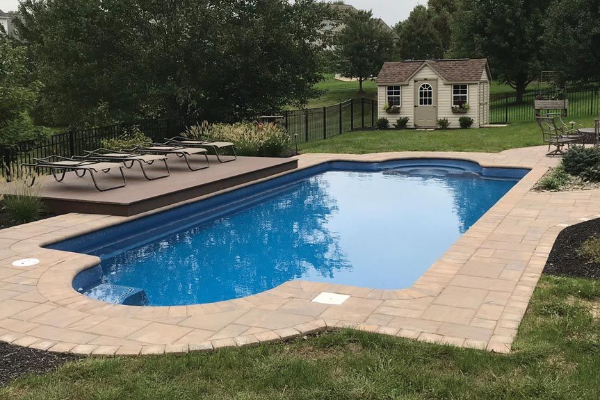 Backyard swimming pool with lounge chairs, stone deck, and a small shed in the background