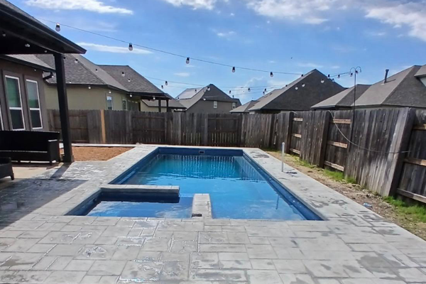 Backyard with a rectangular in-ground pool and raised spa, surrounded by pavers and a wooden fence