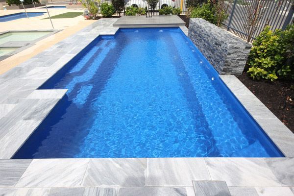 Rectangular blue swimming pool with stone decking and landscaped patio surrounds