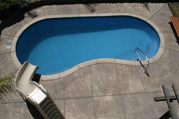 Empty blue swimming pool with a slide and metal ladder on a concrete deck, viewed from above