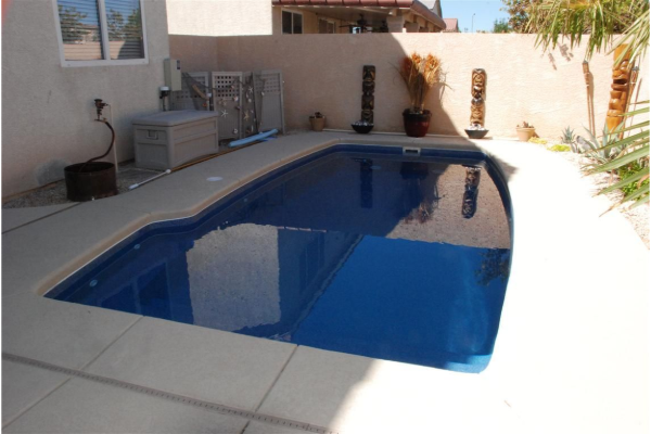Small backyard pool with blue water and a patio, bordered by white concrete walls and plants
