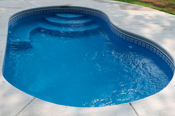 Blue backyard swimming pool with curved shape and light stone deck