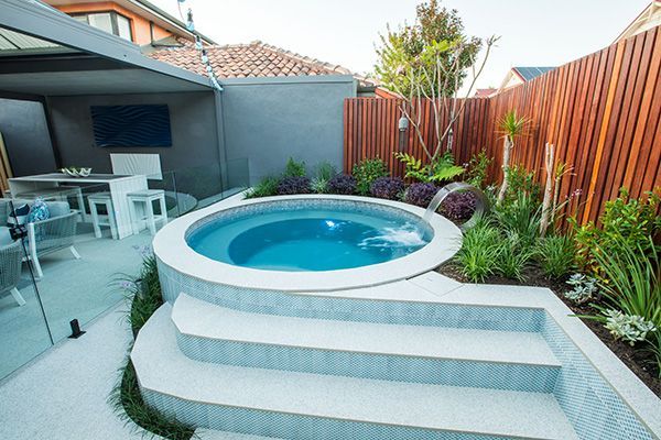 Backyard patio with a small round blue spa and stepped white seating beside landscaped greenery