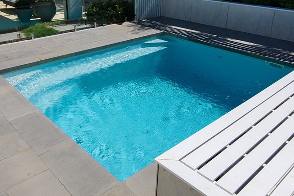 Outdoor swimming pool with blue water and a white lounge chair beside the deck