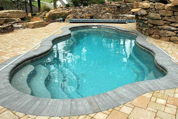 Curved backyard swimming pool with turquoise water and stone deck, viewed from above