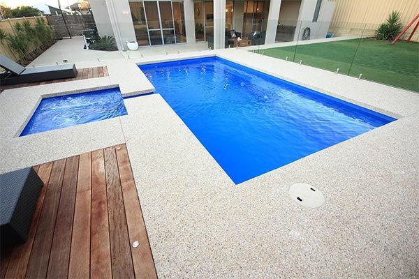 Modern backyard with a blue swimming pool, spa, and wooden deck beside a house