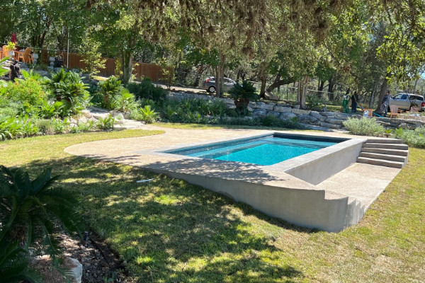 Rectangular backyard pool with steps, surrounded by lawn, trees, and landscaped greenery