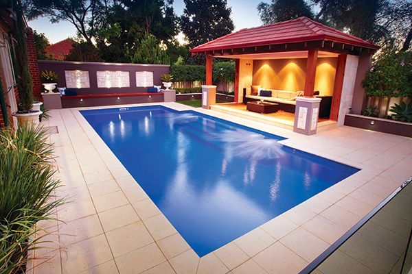 Modern backyard with a rectangular swimming pool and covered patio at dusk