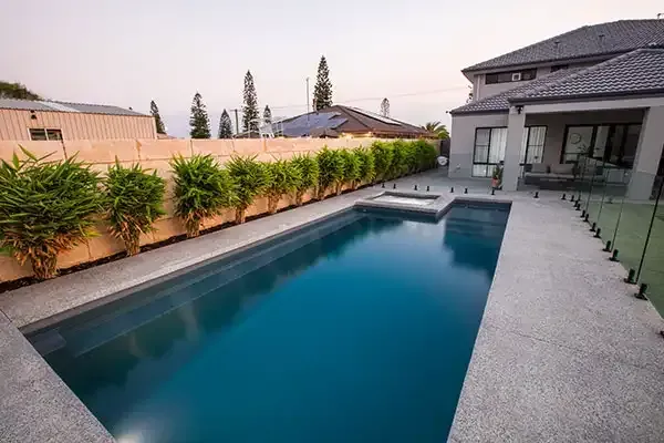 Modern backyard with a rectangular swimming pool, patio, and privacy hedges at sunset