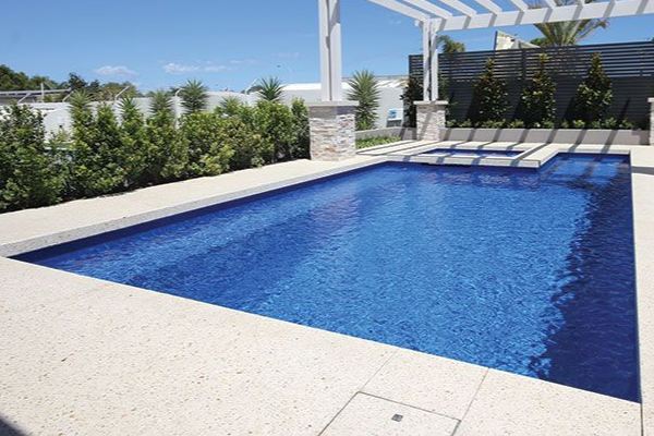 Modern backyard swimming pool with blue water, white deck, and pergola seating area