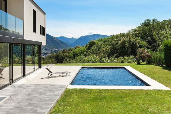 Modern house with a backyard pool, patio loungers, green lawn, and mountain view